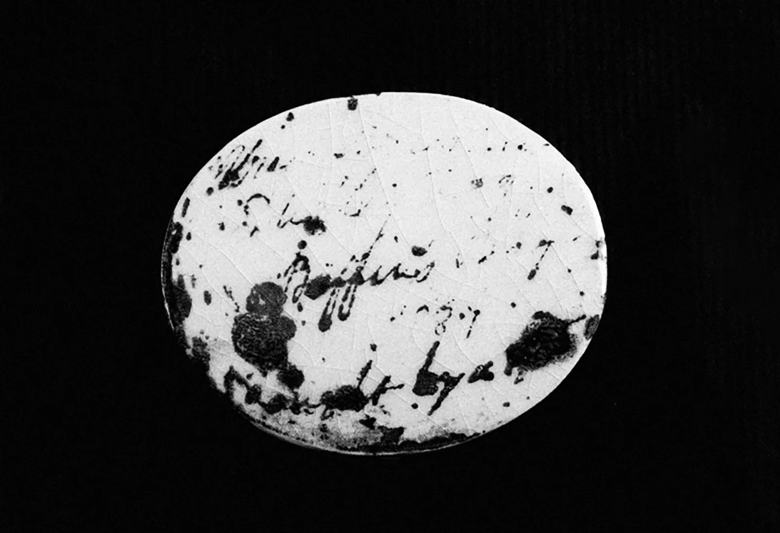 Galet en céramique blanche imprimé d’écritures noires, sur fond noir